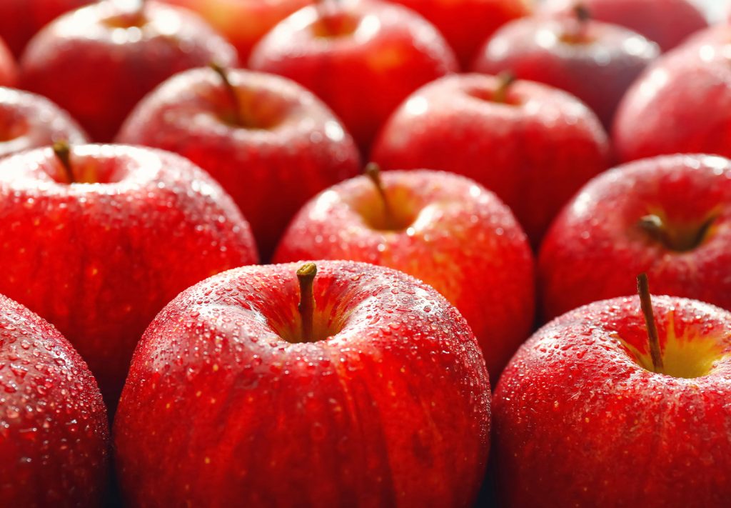 Close-up of freshly washed red apples glistening with water droplets, arranged together showing their glossy skin and stems.