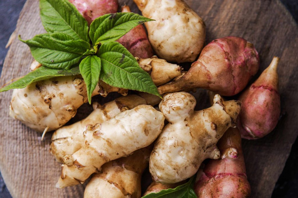 Freshly harvested ginger root and red potatoes arranged on a wooden surface with fresh mint leaves.