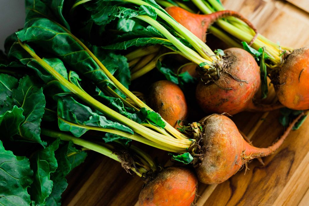 Bunch of fresh beetroots with vibrant green stems and leaves arranged on a wooden cutting board