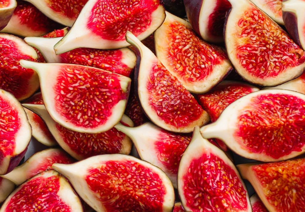 Close-up overhead view of freshly sliced red figs arranged together, showing the vibrant pink and red flesh with cream-coloured skin.