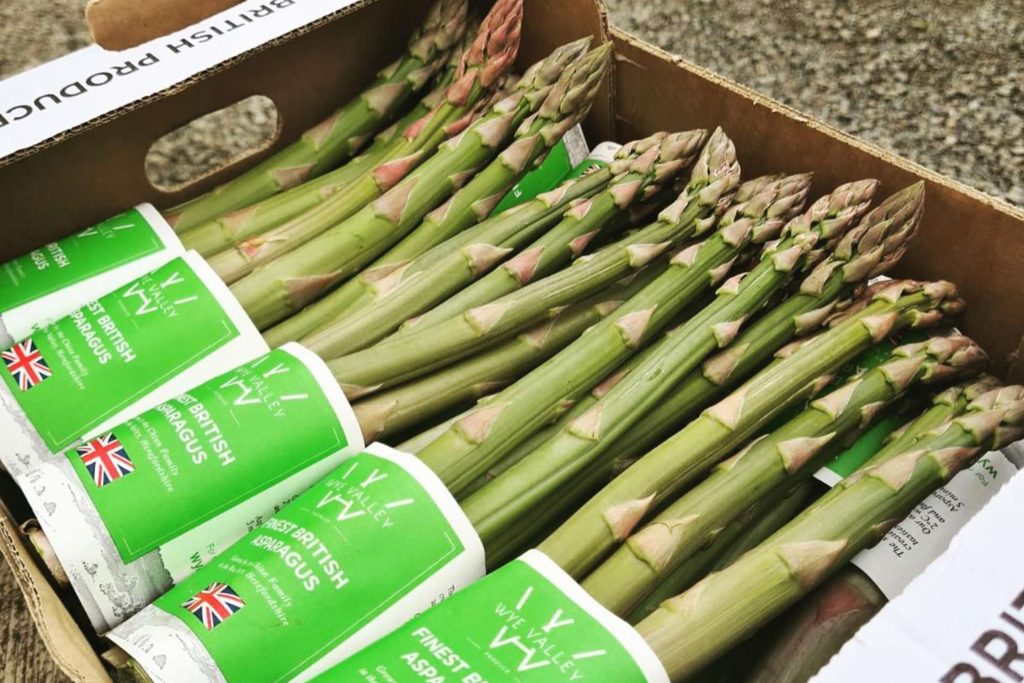 A cardboard box containing fresh green asparagus spears with British flag labels on white and green packaging bands.